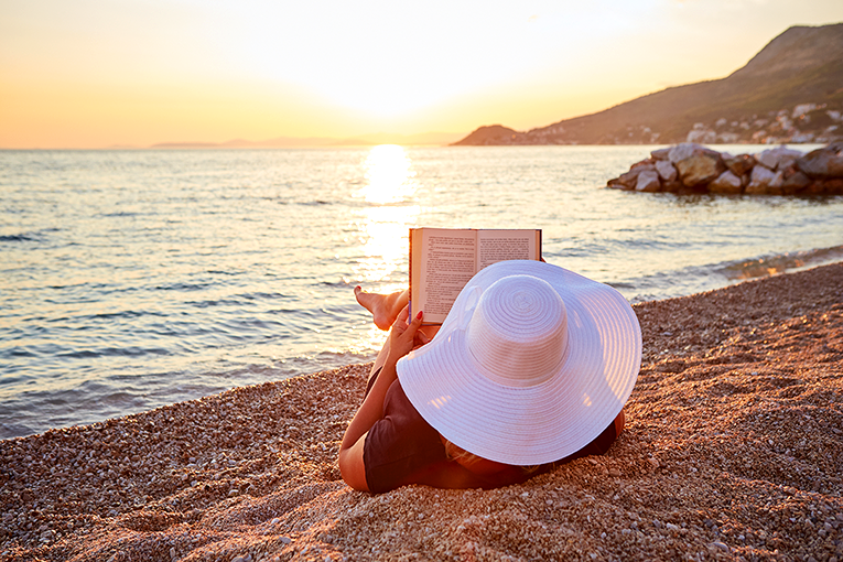 Bild på kvinna som läser en bok i solnedgången på en strand