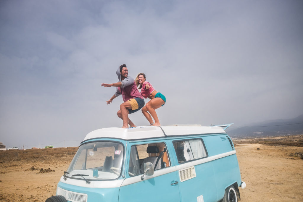 Spain, Tenerife, laughing young couple standing on car roof enjoying freedom